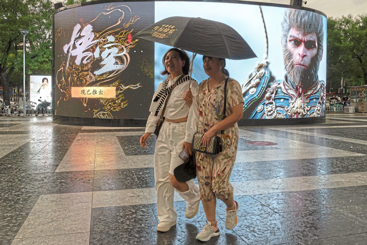 Women share an umbrella as they past an ad promoting the blockbuster Chinese video game 'Black Myth: Wukong' in Beijing. 