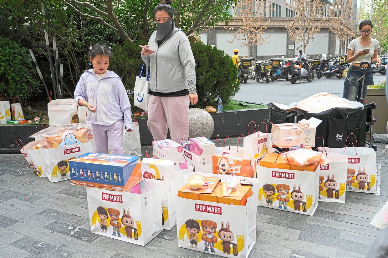 Shoppers pass by bags of Labubu merchandise from PopMart outside a mall in Beijing. 