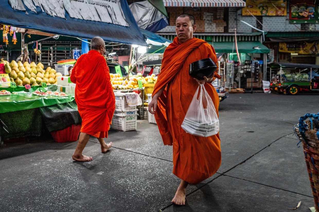 Buddhist monks collect alms as they walk past fruit stalls at Mahanak Market in Bangkok early on Monday, April 20, 2026. -- Photo by ANTHONY WALLACE / AFP