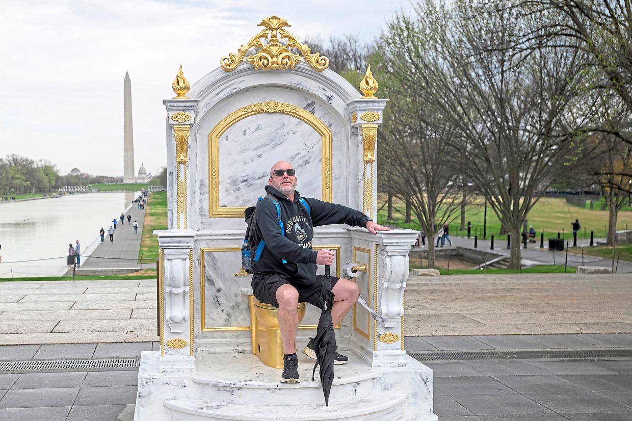 After a weekend of ‘No Kings’ protests, a man poses beside protest artwork titled ‘A Throne Fit for a King’ – a toilet-seat throne installed near the Lincoln Memorial in Washington, DC. — AP