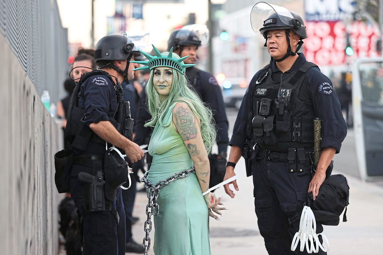 LAPD officers detaining a protester dressed as Lady Liberty in chains after clashes near the Metropolitan Detention Center during the ‘No Kings’ protest in Los Angeles, California. — AP