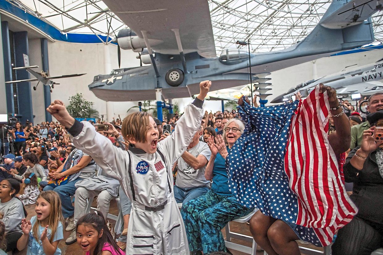 A young boy dressed as an astronaut cheering alongside a woman waving a flag as they and others watch a live broadcast of the Artemis II crew’s return during a splashdown watch party at the San Diego Air and Space Museum in California. — AFP