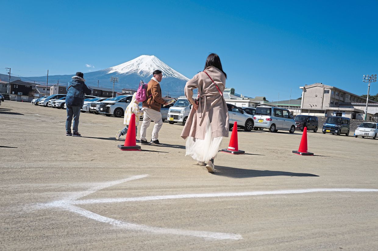 Seeing the sights: Foreign visitors looking at Mt Fuji from a car park near Shimoyoshida Station; (below) a security guard guiding tourists near the entrance of Arakurayama Sengen Park. — AP 
