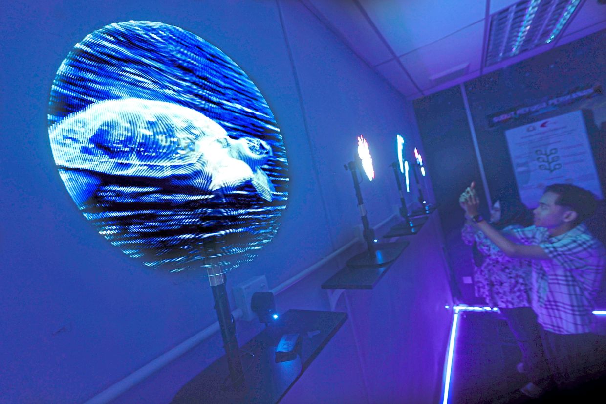 Visitors to Mersing Marine Park Gallery observing fish and jellyfish movements through 3D holographic fans which project lifelike images of marine creatures.