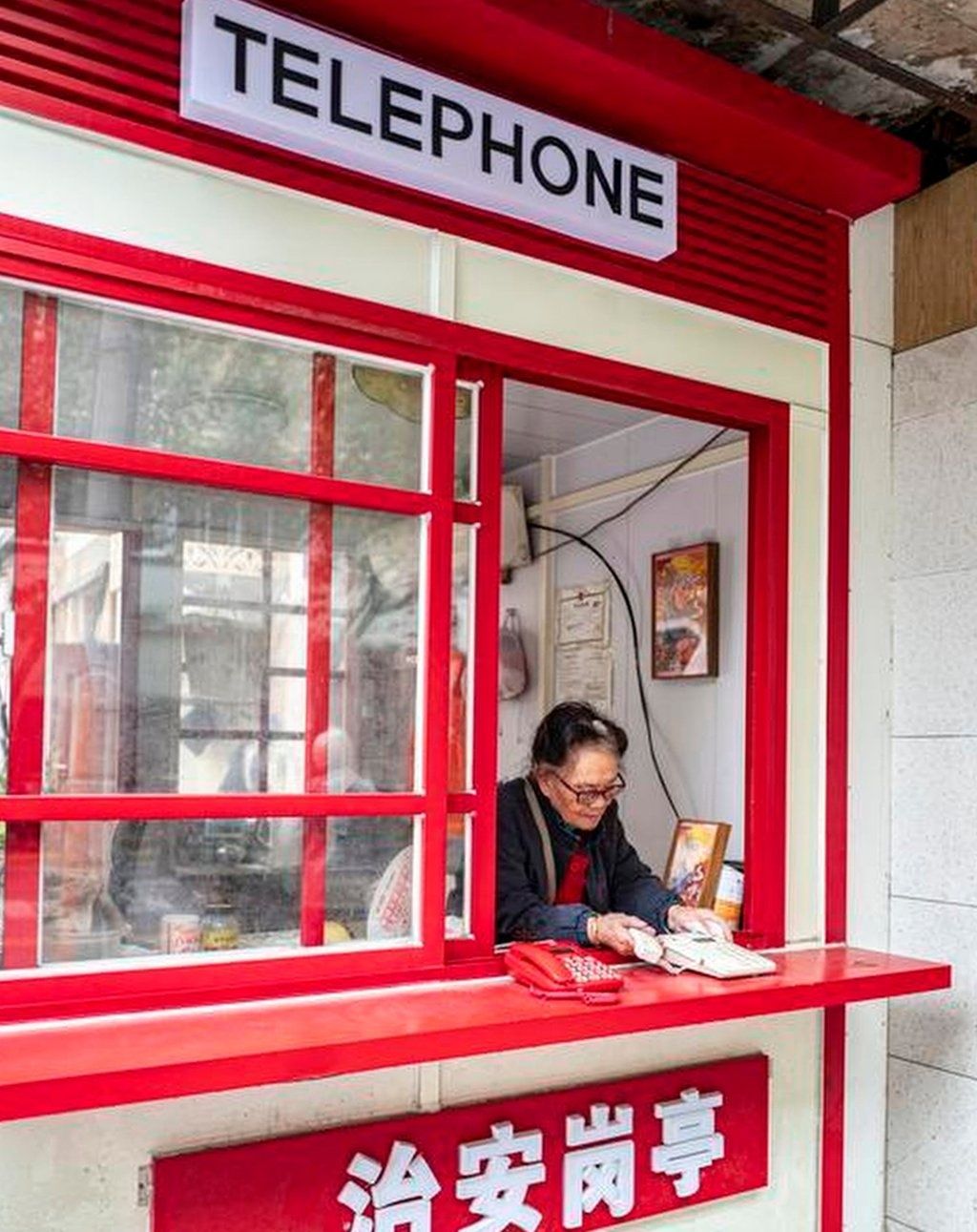 Shen Yuxiu, above, working at the bright red-coloured phone booth in Shanghai. - Photo: QQ.com