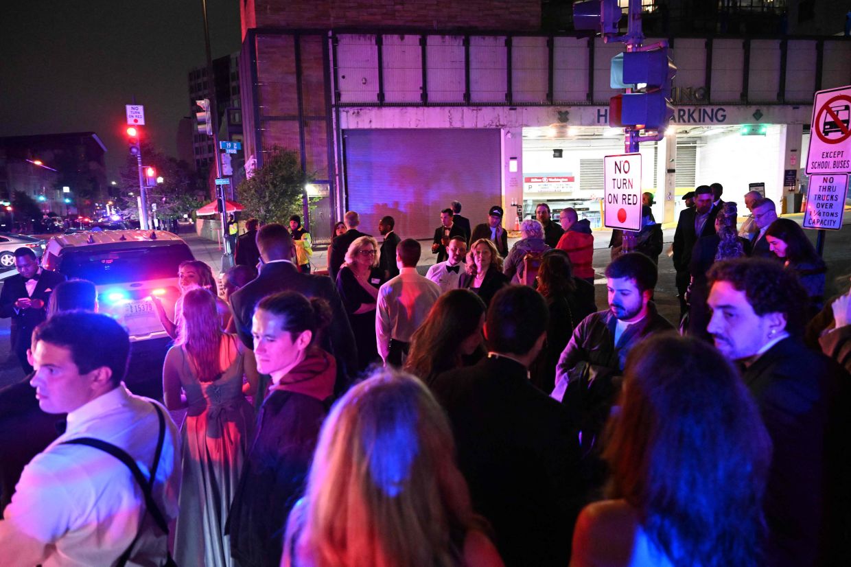 Guests escorted out the back of the hotel stand nearby after leaving after shots were fired during the White House Correspondents' dinner at the Washington Hilton in Washington, DC, on April 25, 2026. Shots were fired as US President Donald Trump attended a media gala in Washington on Saturday night, with the gunman detained at a screening area just outside the hotel ballroom where hundreds of guests had gathered. (Photo by Roberto Schmidt / AFP)