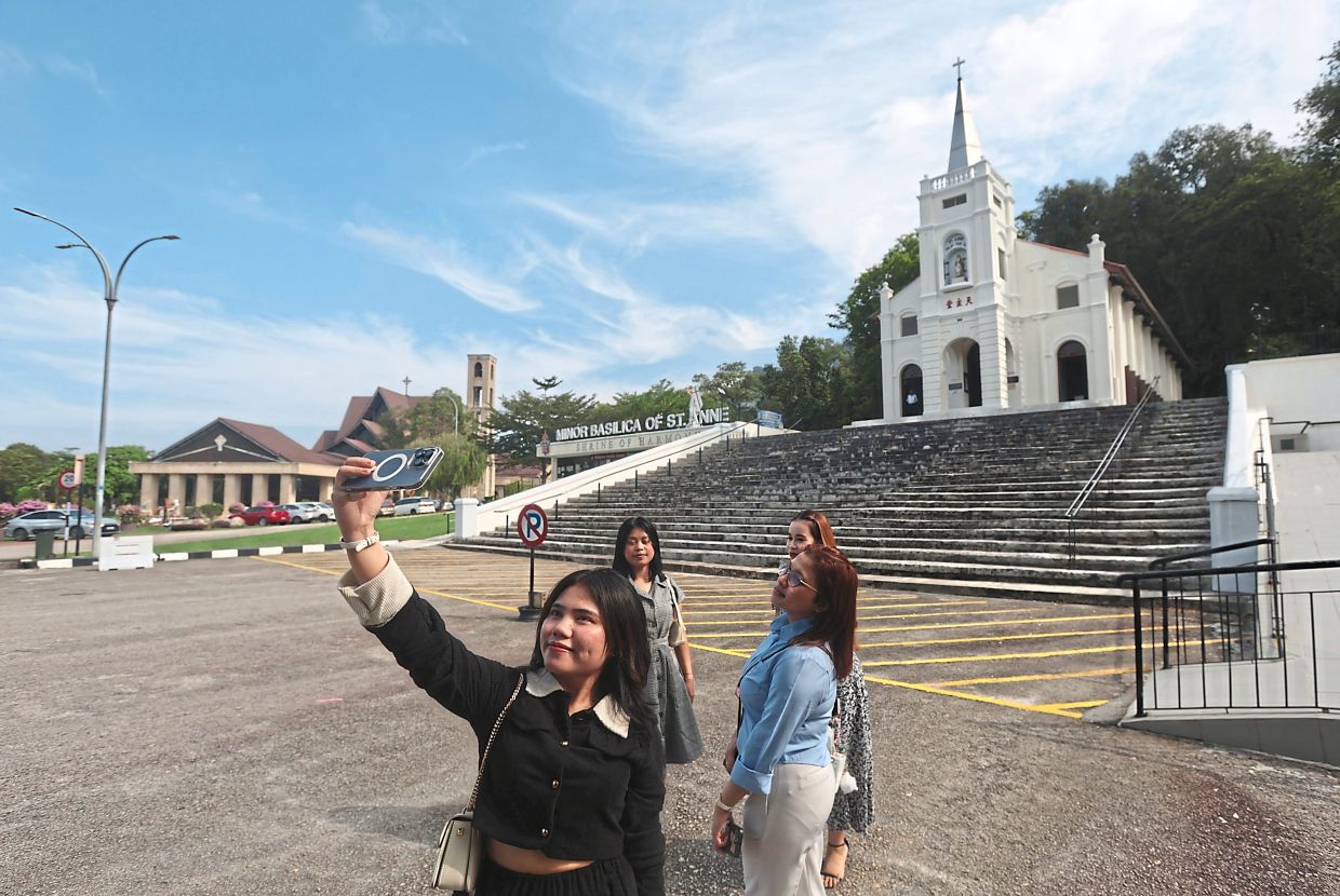 Charms beyond the island: Visitors exploring Minor Basilica of St Anne in Bukit Mertajam, Penang, which includes the old church from 1888 at the top of the stairs and the Minangkabau-inspired structure (left) opened in 2002. — ZHAFARAN NASIB/The Star