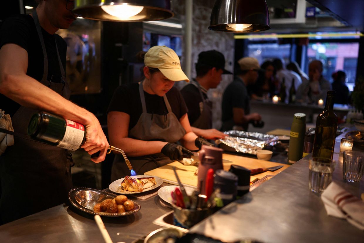A cook prepares rotisserie chicken with potatoes during dinner service at the French restaurant Gigi's