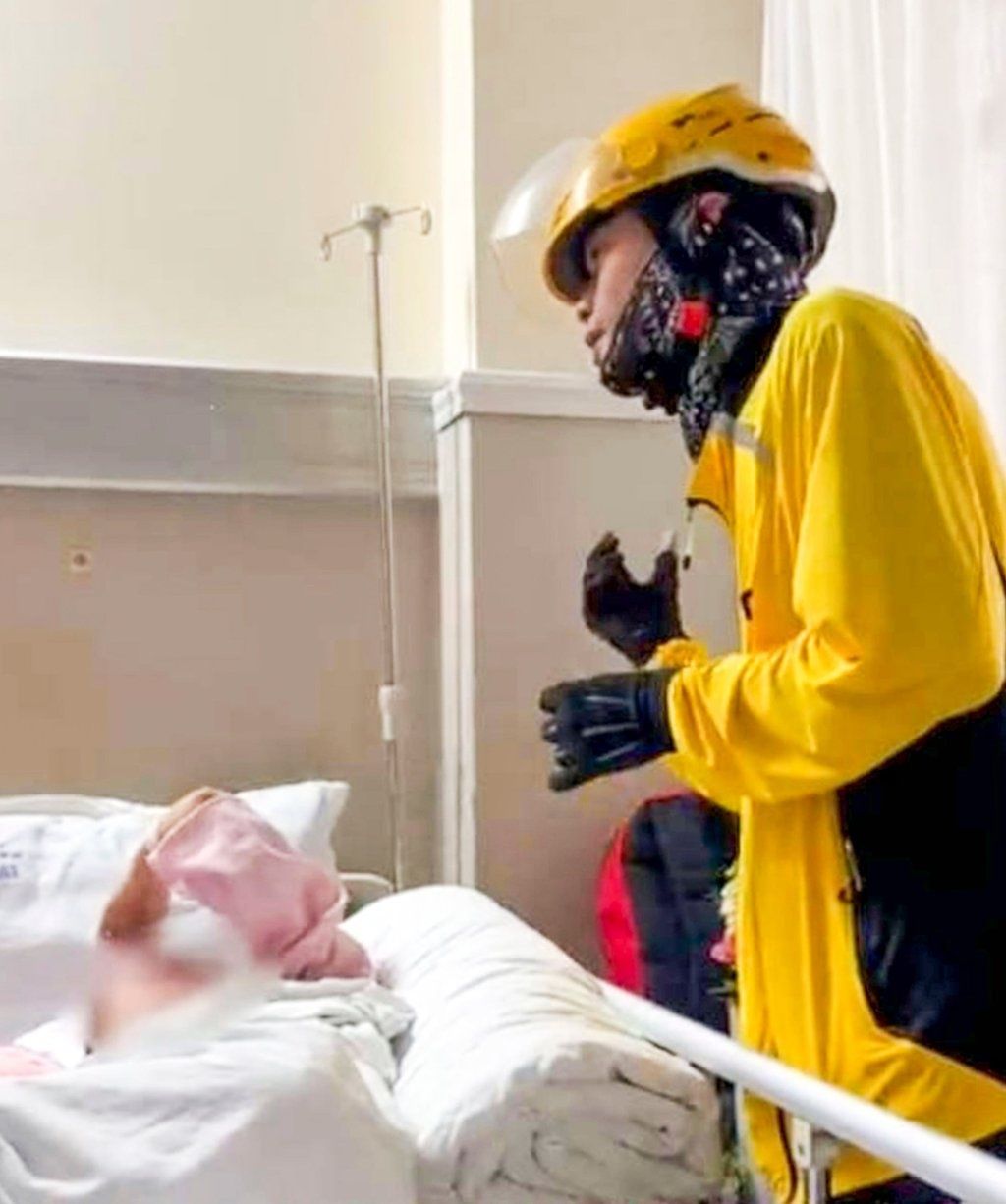 A delivery rider in full working gear chats to Li as she lies in her hospital bed. - Photo: Douyin