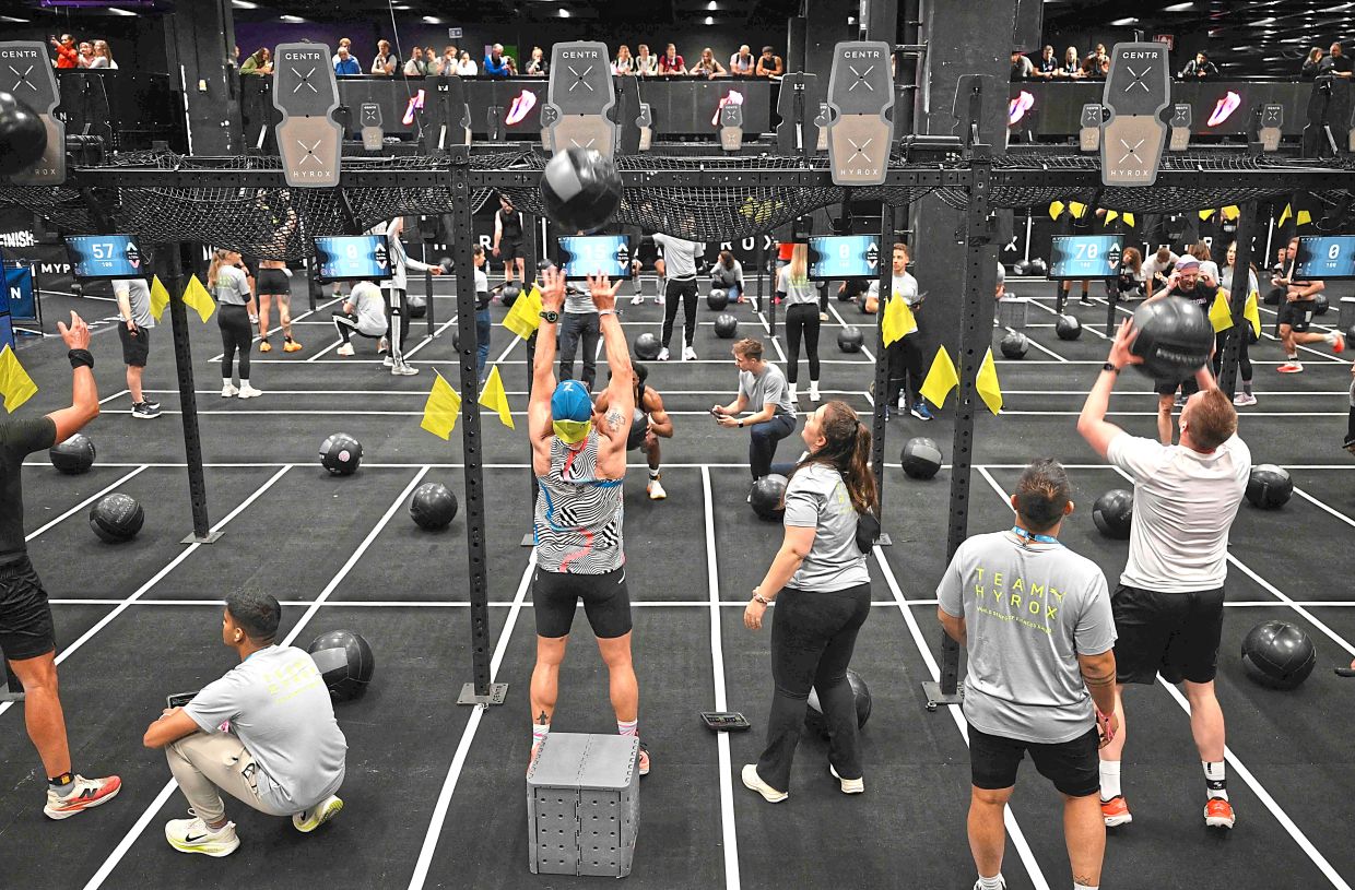 Participants at the final workout station (wall balls) where they have to combine a squat and an overhead throw of a weighted ball against a wall. — AFP 