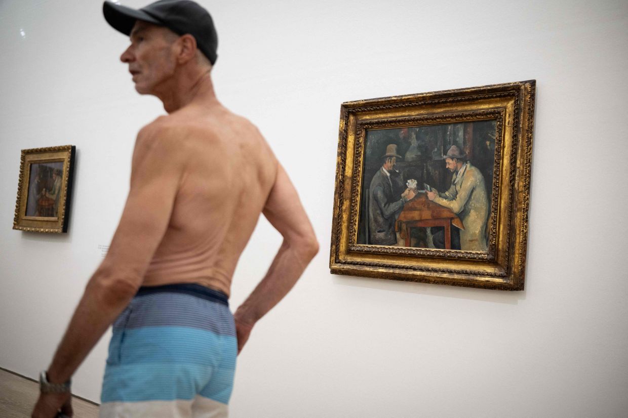 A visitor wearing a swimsuit walks past the painting called 'The Card Players' (1893-1896) by French painter Paul Cezanne during the experience called 'bathers' day' at the Beyeler Foundation in Riehen, northern Switzerland. Photo: AFP 