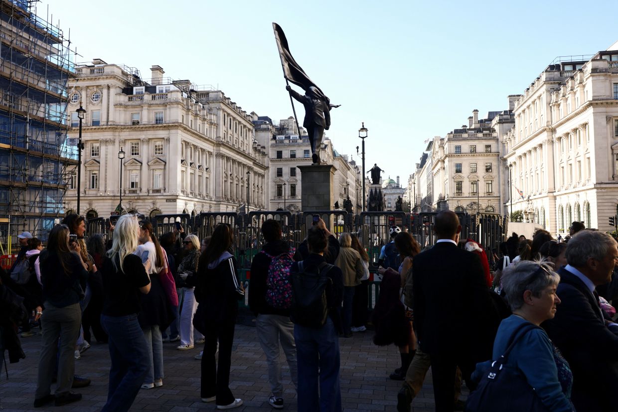 People gather next to a statue depicting a person stepping off the plinth while carrying a flag covering his face by Banksy in central London. Photo: Reuters