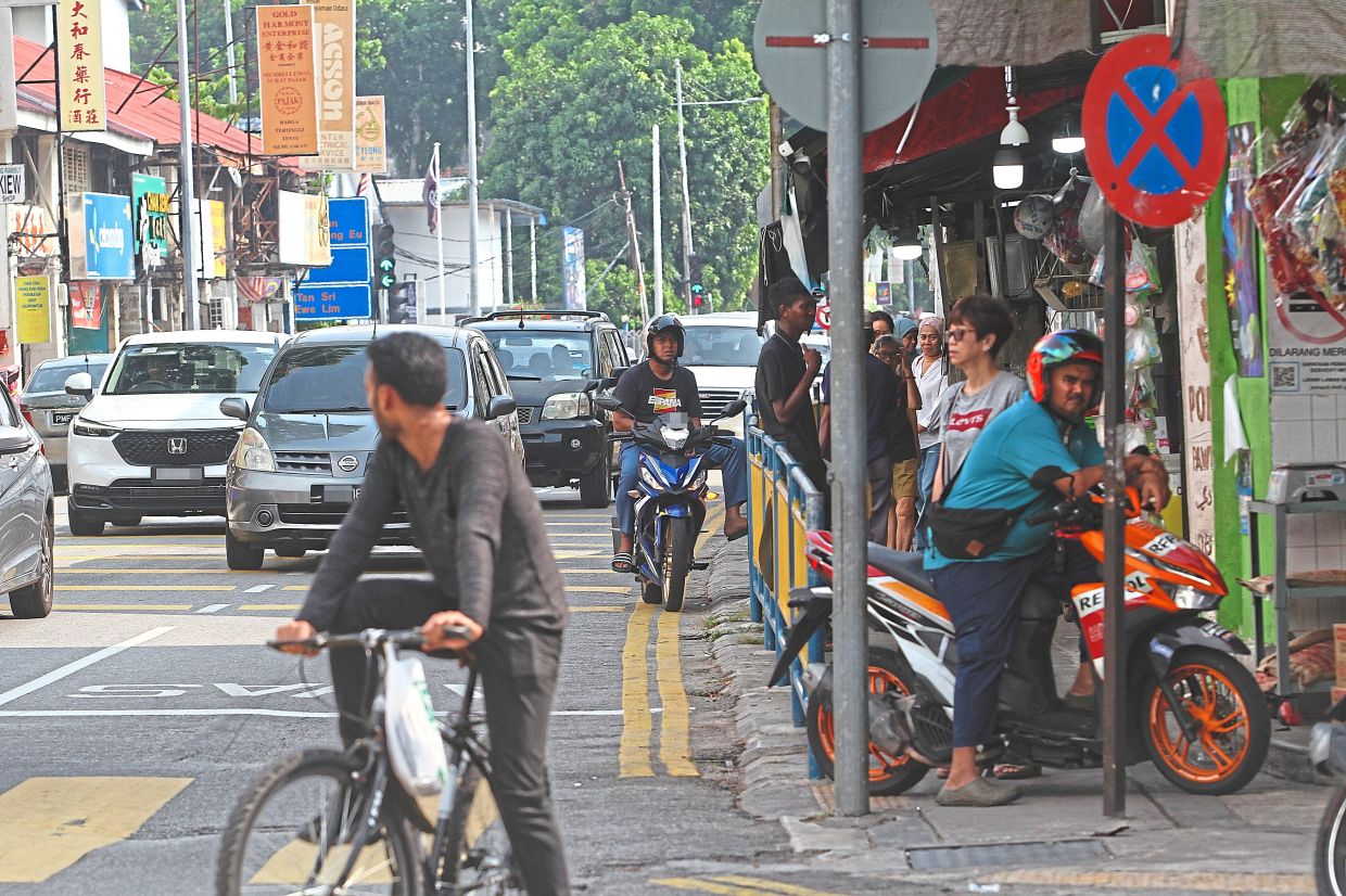 Motorcyclists stopping by the roadside and on the five-foot way along Jalan Jelutong. By doing so, they are blocking traffic and hindering pedestrians.