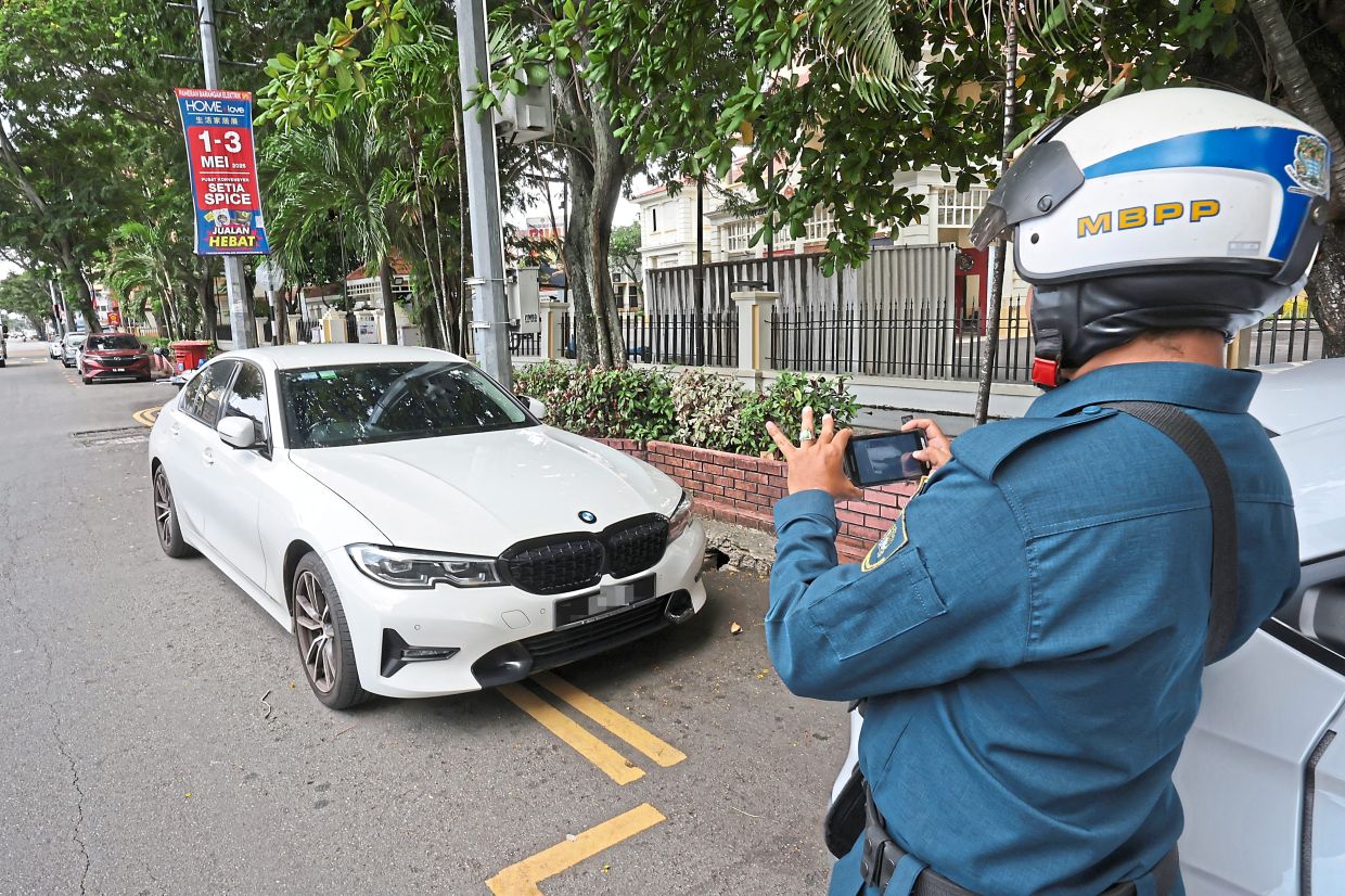 An MBPP enforcement officer taking photo evidence of a car parked on double yellow lines. — CHAN BOON KAI/The Star