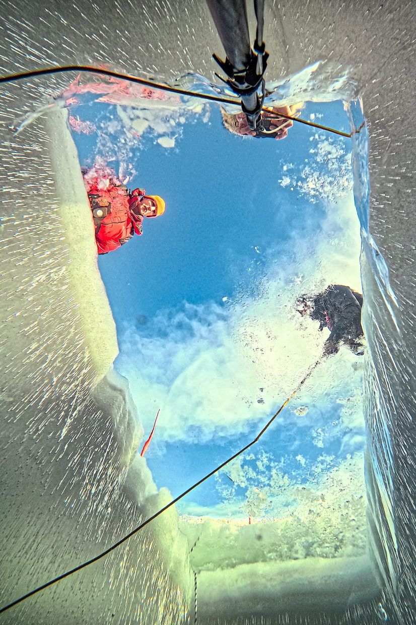 Participants look into an ice hole as a diver descends beneath the surface.