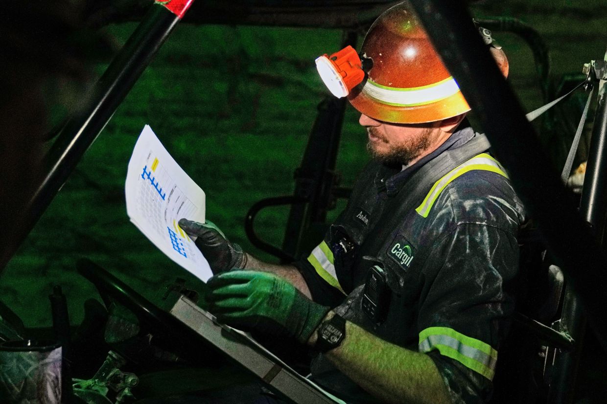 The absolute darkness of the mine is broken as supervisor Andrew Adkins uses a headlamp to look over a map of drilling sites at the Cargill Salt Mine.
