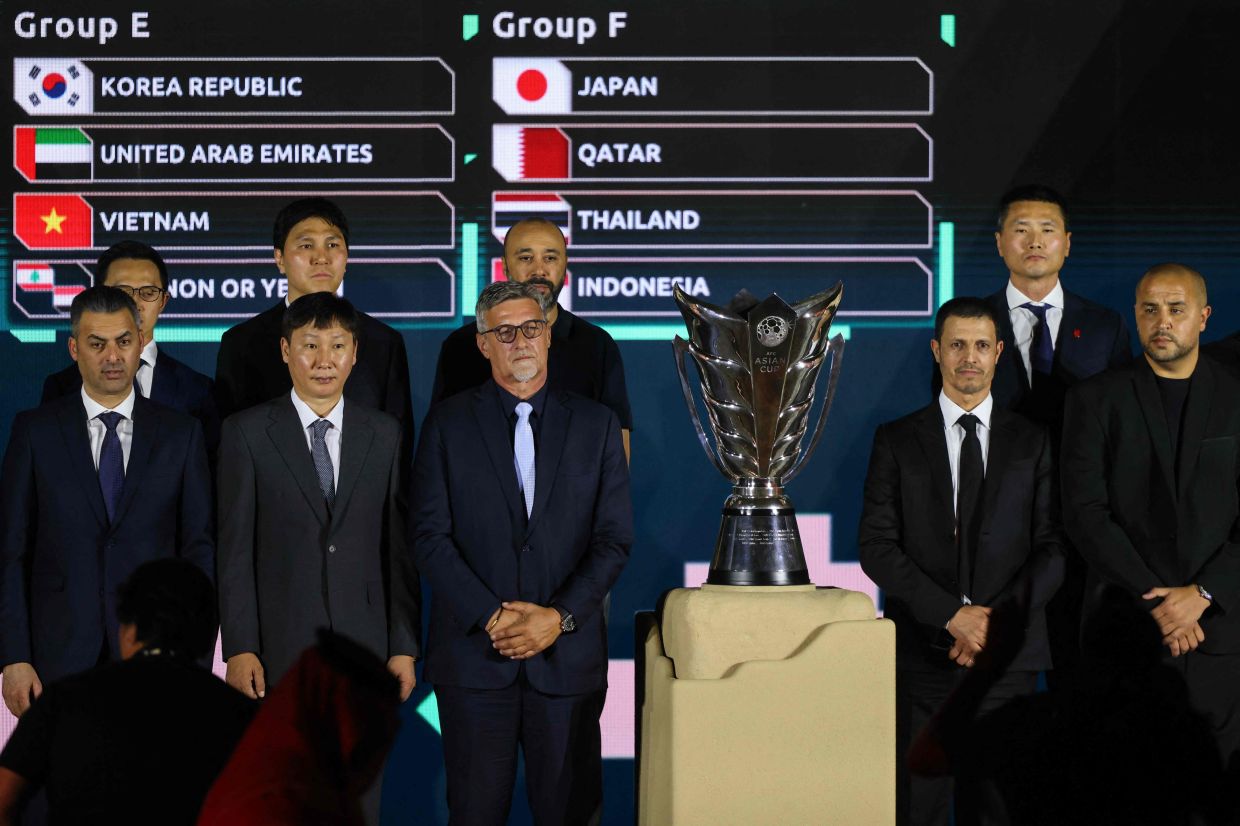 Coaches of Asian national football teams pose next to the trophy and in front of a screen showing the results of the final draw for the 2027 AFC Asian Cup during a ceremony in Diriyah, on the outskirts of Riyadh, on May 9, 2026. The 19th edition of the Asian Cup is scheduled to take place from January 7 to February 5 next year in Saudi Arabia. -- Photo by Fayez Nureldine / AFP