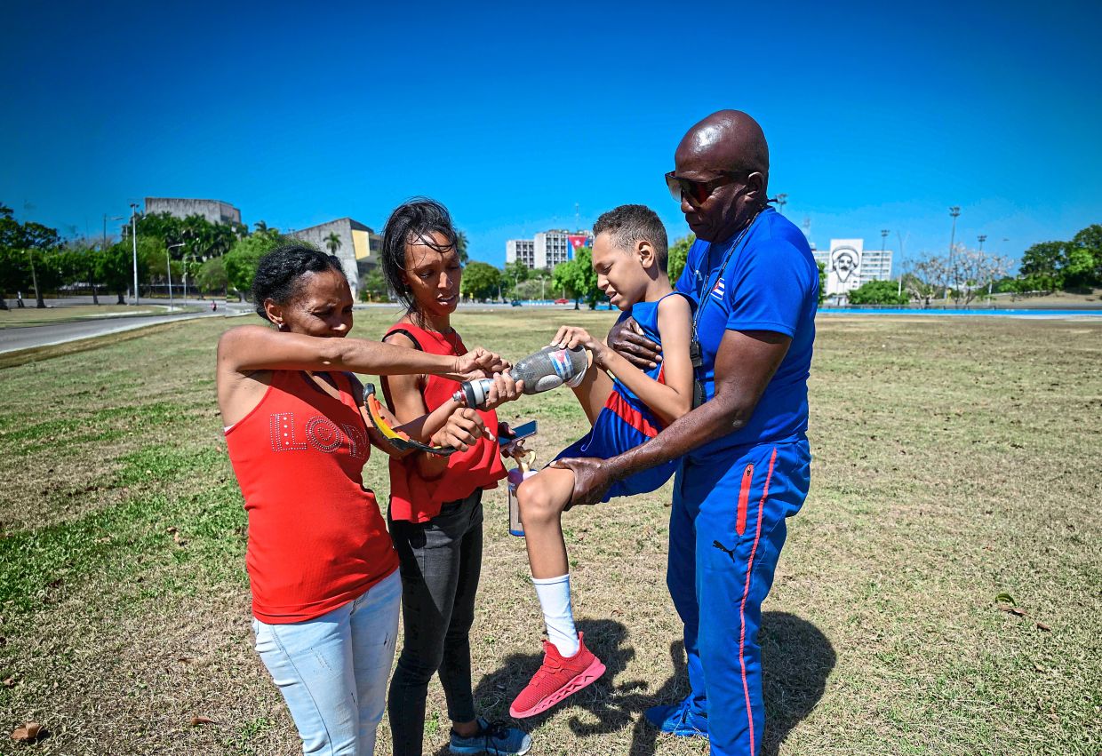 Juan Jose is carried by his pentathlon trainer Albert Luis Campbell (right) as his grandmother Suleimi Licea Rodriguez (left) and his mother Sheila G adjust his prosthesis. Photo: AFP