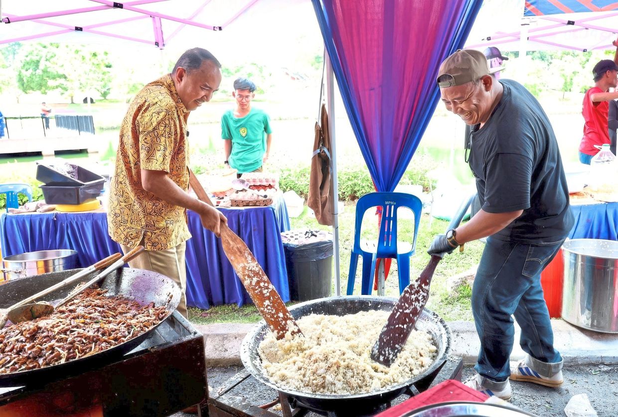 Johor housing and local government committee chairman Datuk Mohd Jafni Md Shukor (left), who is also Bukit Permai assemblyman, stirring fried rice during an open house at Tasik Hutan Bandar MPKu in Kulai.