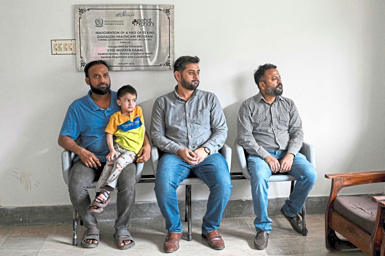 Remote care: Muhammad Adil (left), waiting for an online medical consultation for his son at a Sehat Kahani clinic in Karachi. — AFP