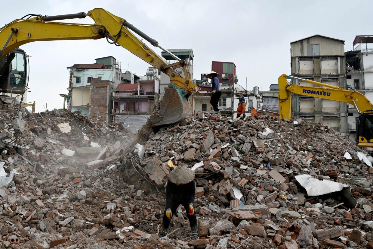 Workers (centre) collect scrap metal from the rubble of residential buildings as excavators are seen at a demolition site to make way for an expanded road network in Hanoi on Monday, May 18, 2026. -- Photo by Nhac NGUYEN / AFP
