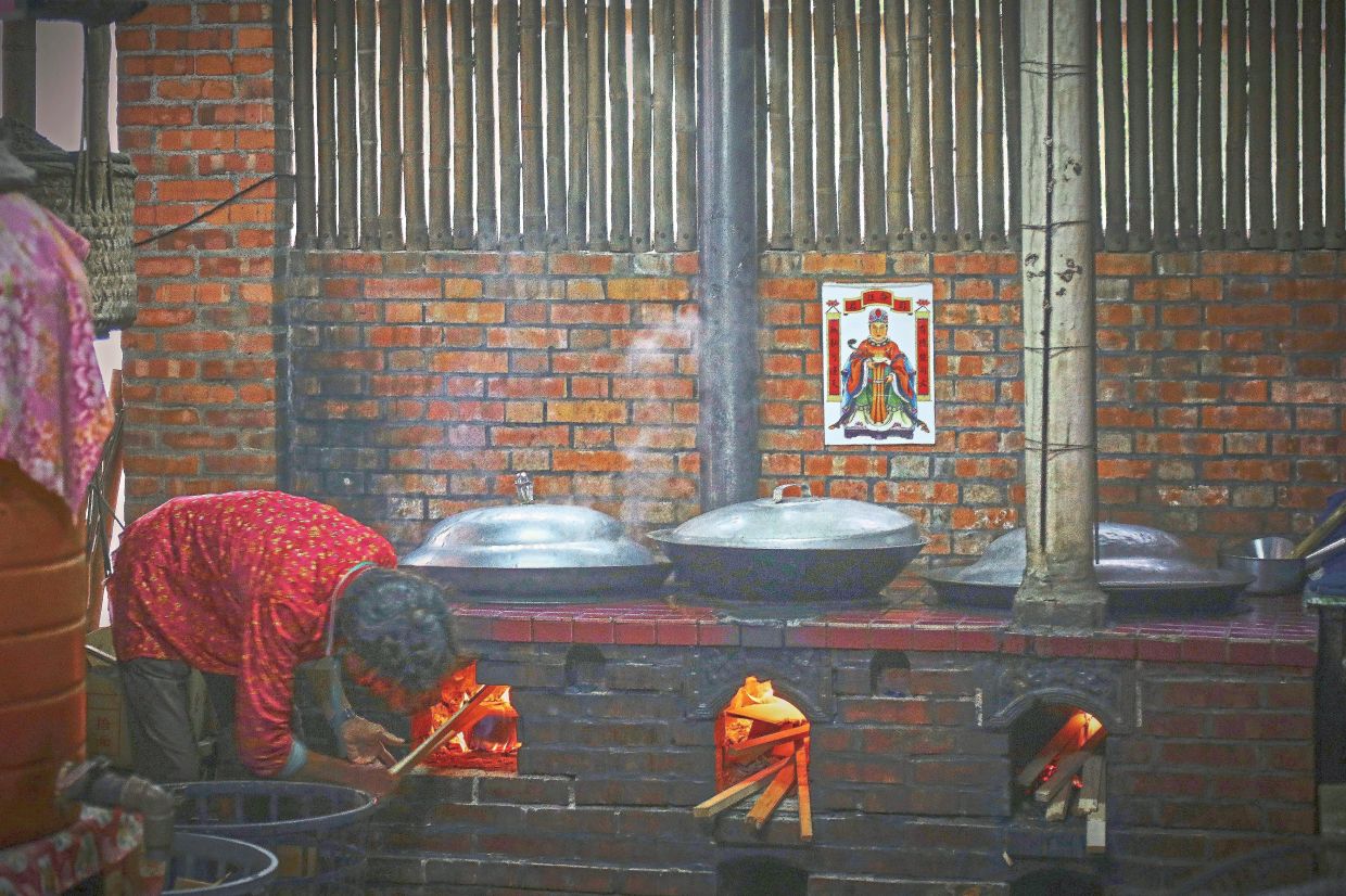 A woman checking on large metal pots sitting over open fires in a traditional kitchen at Dongluo River Leisure Farm, where coal-fired brewing and ‘rice harvest meals’ evoke time-honoured rural cooking traditions. Photos: YAP CHEE HONG/The Star
