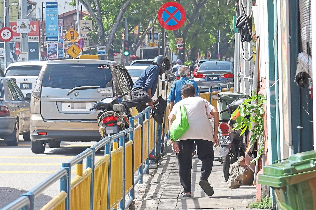 A motorcyclist leaving his vehicle on the roadside and climbing over the pedestrian barricade for quick access to the shops in Pulau Tikus. 