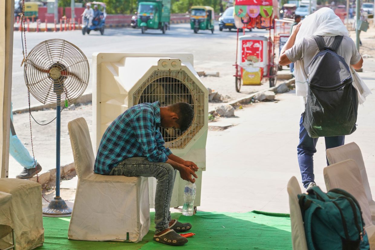 A man sitting in front of a water cooler at a roadside cooling station set up by the government to provide relief for people from the intense summer heat in New Delhi on May 20. - AP