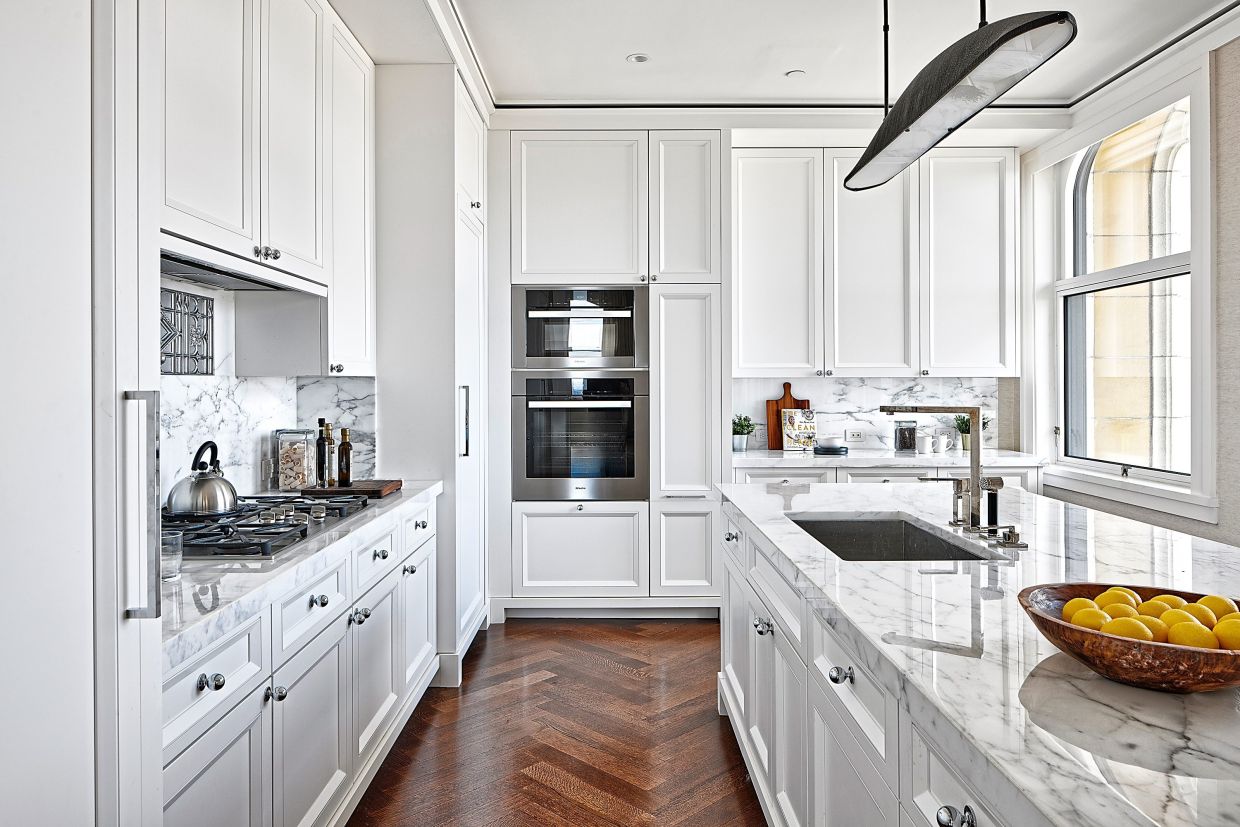 A kitchen with white traditional cabinetry, paired with a marble countertop with grey veining.