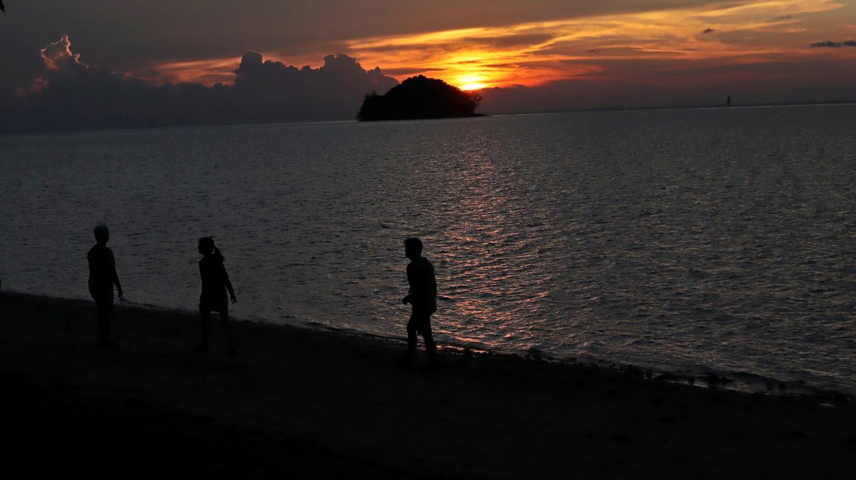 Children playing along the shoreline of Pulau Libaran during sunset.