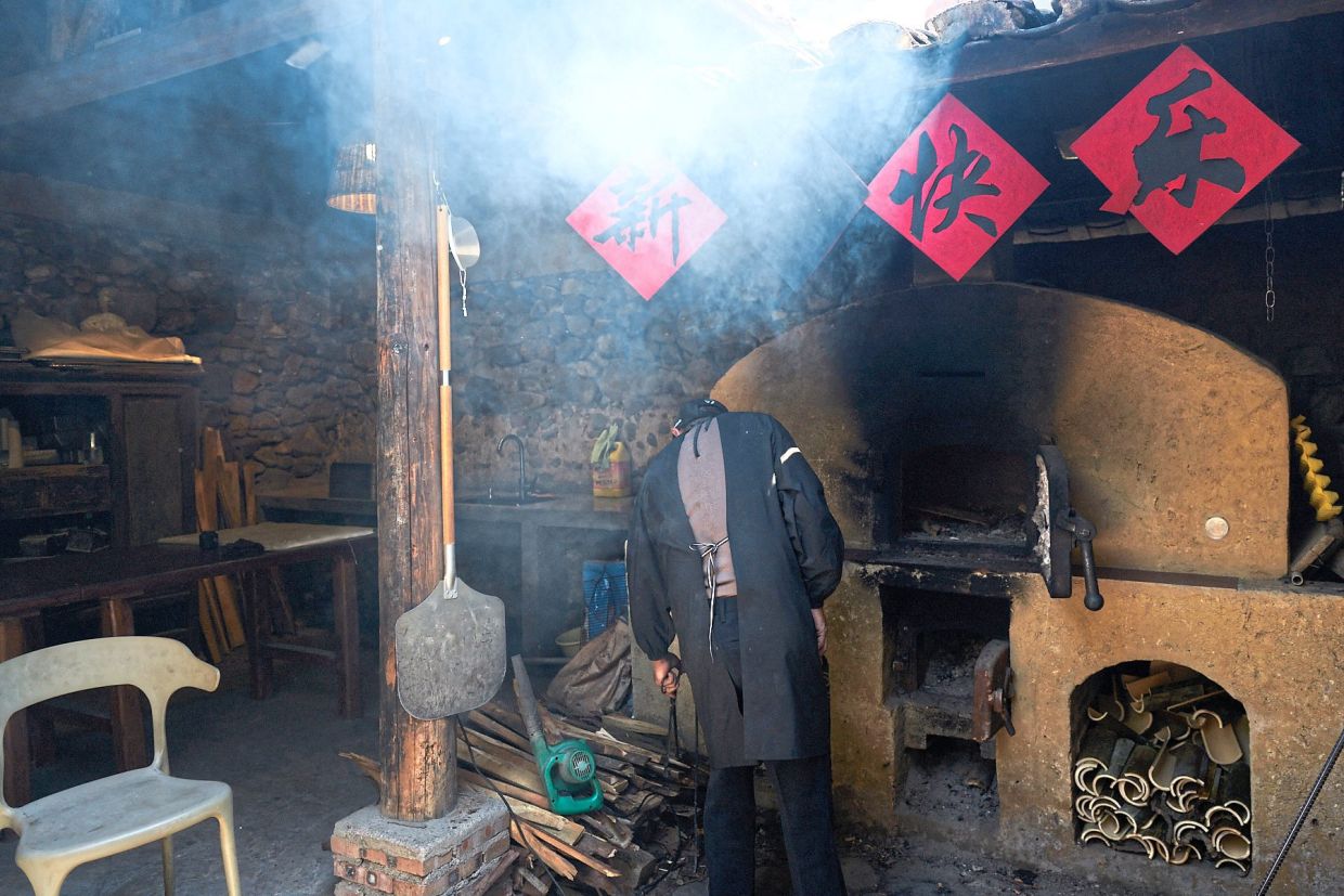 A man baking bread the traditional way, using an old earthen oven in Xitou Ancient Village.