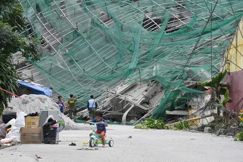 A child riding a tricycle next to a collapsed building in Angeles City, north of Manila, where at least 12 people were believed to be buried. - Photo: AFP