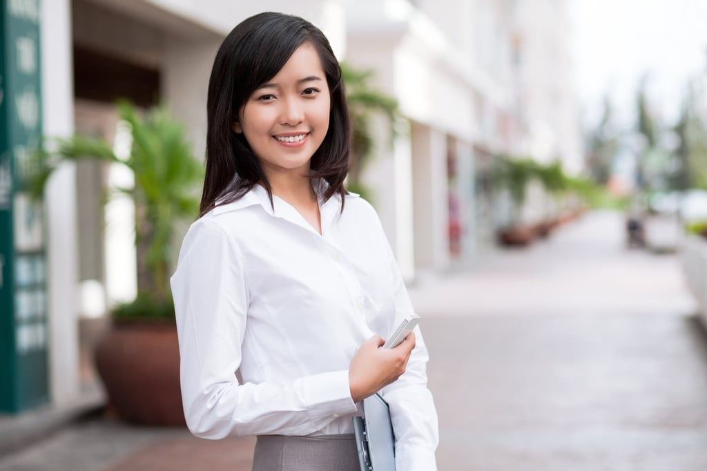 A young, smiling woman holds a mobile phone. Many Asian women consider the double eyelid a standard of beauty. -- Photo: Shutterstock/SCMP