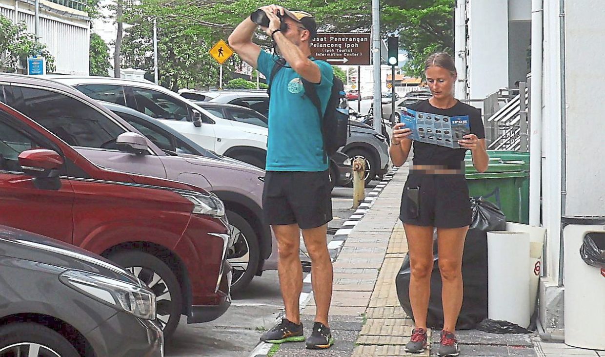 Tourists with binoculars and map looking out for attractions while on the Ipoh Heritage Walk.
