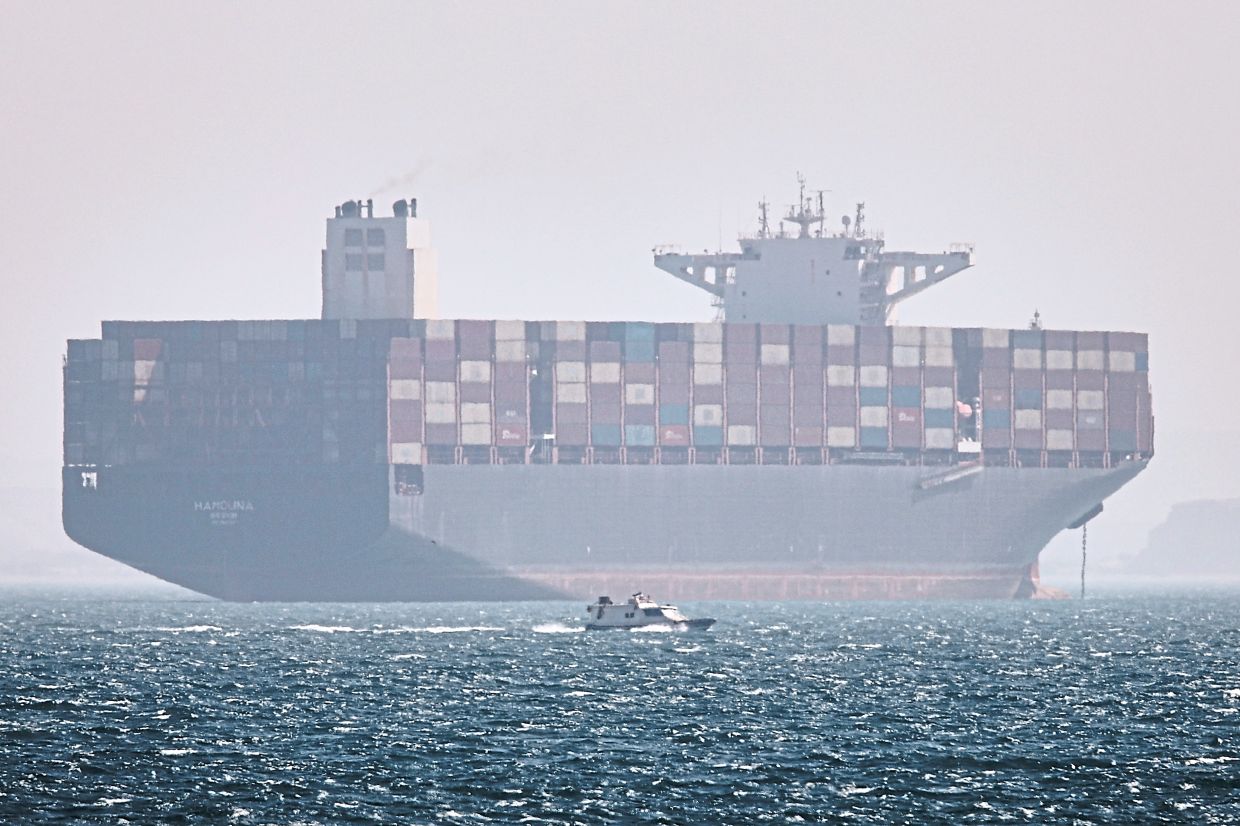 A container ship sits at anchor as a small motorboat passes in the foreground in the Strait of Hormuz off Bandar Abbas, Iran.