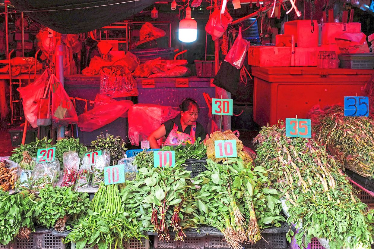 A vendor sits next to her vegetable stall at a fresh market in Bangkok, Thailand. — Reuters