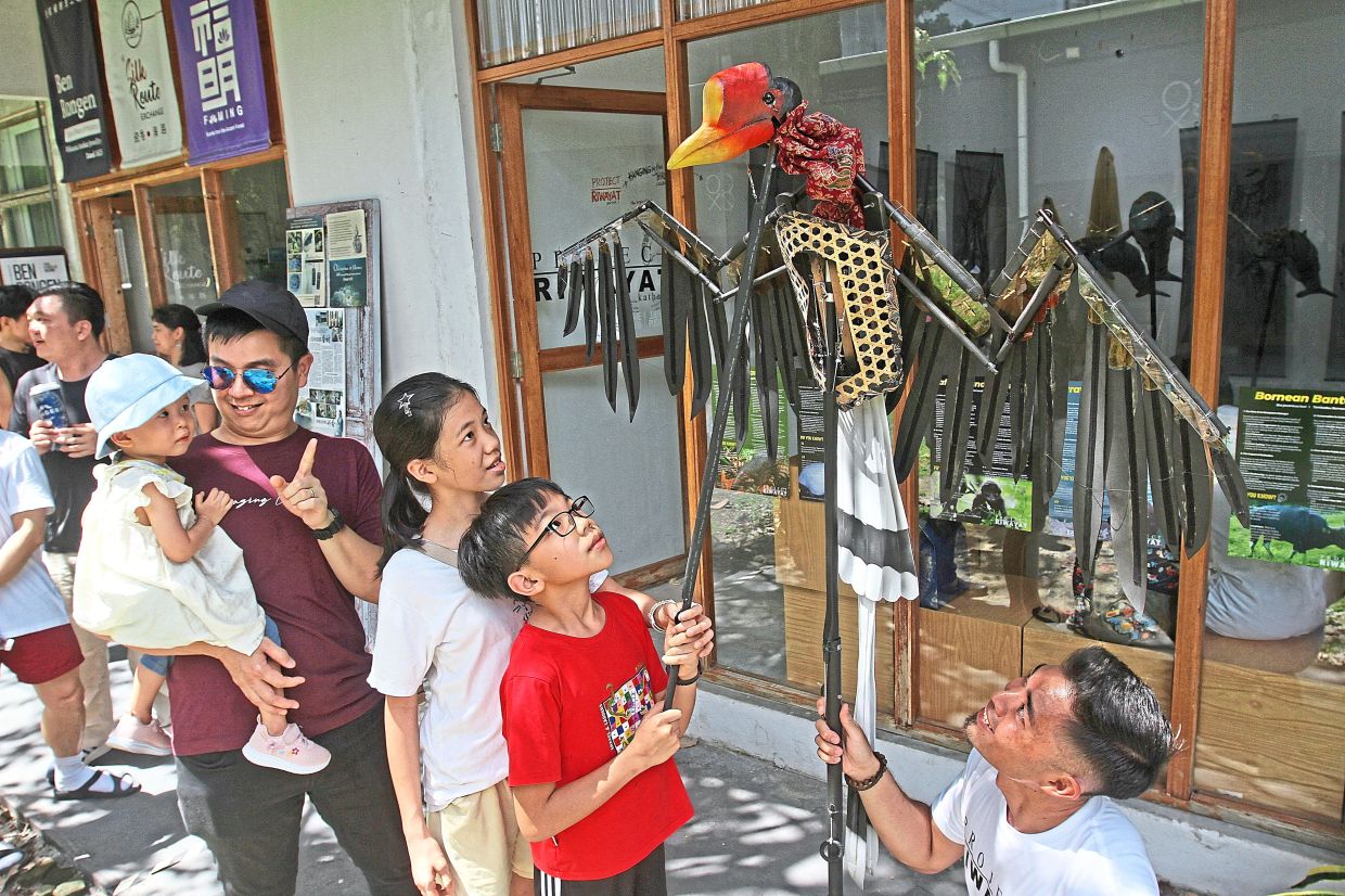 Young visitors with Bright (holding puppet) looking at the helmeted hornbill puppet from Wildlife Encounters.