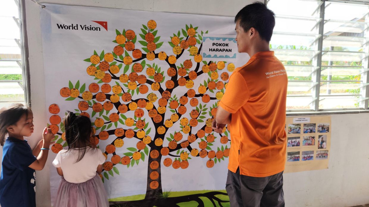 Lai (right) looks on as kids write down their hopes and dreams for the future during the farewell celebration in Tulid. Photo: World Vision Malaysia