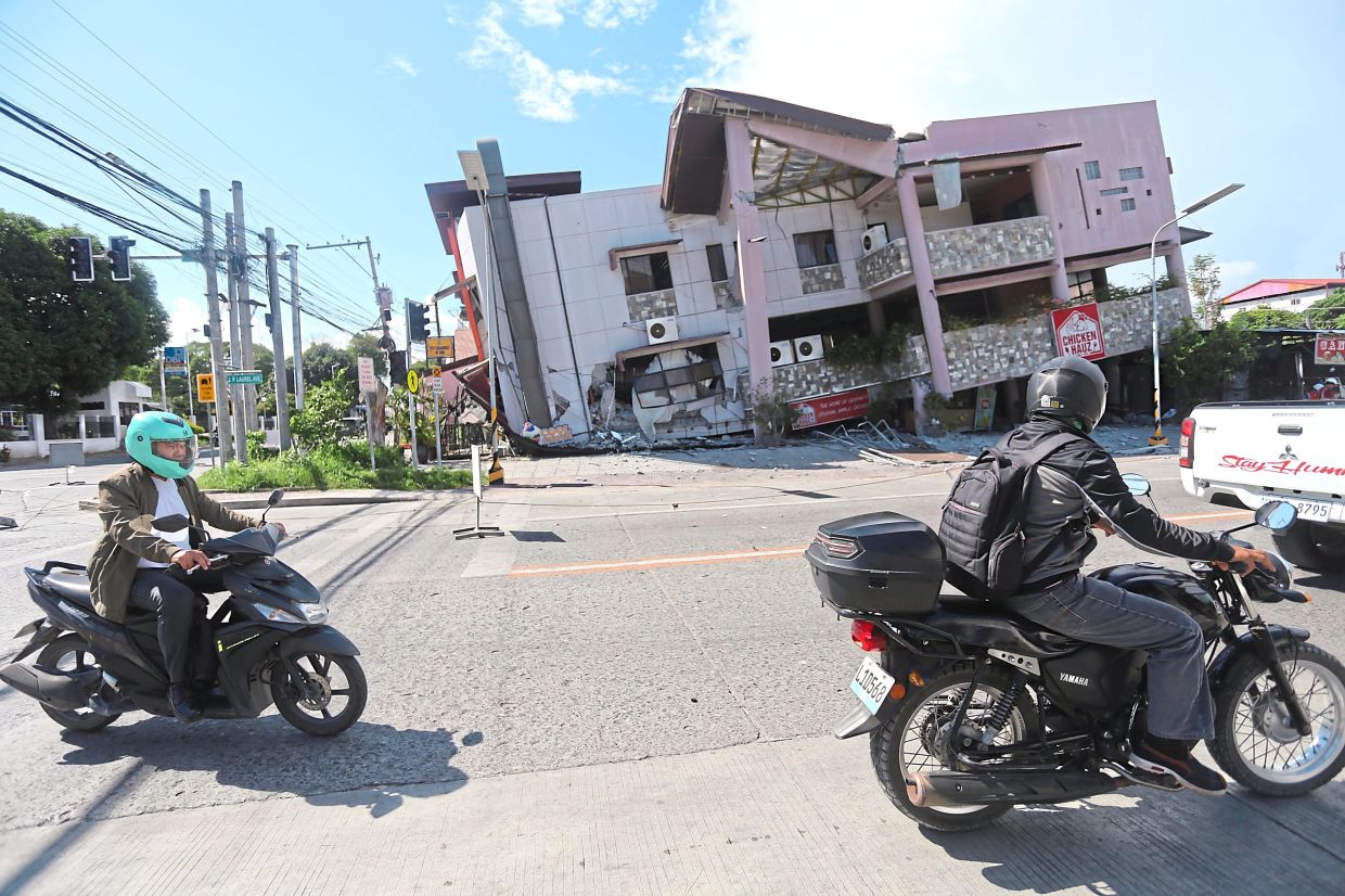 Precarious situation: People on motorcycles passing by a collapsed structure after an earthquake in General Santos. — AP
