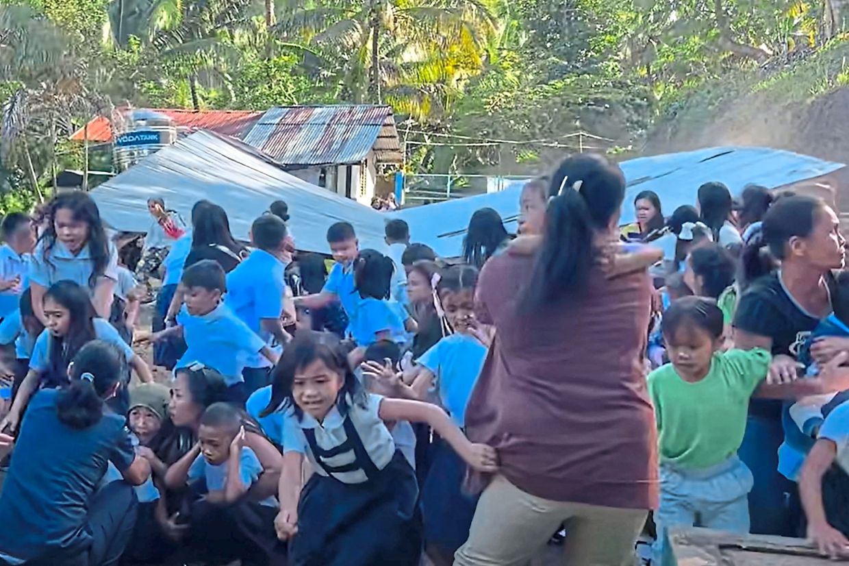 Widespread panic: A screencap of footage showing children huddled in a field reacting as a structure in the background collapses during the earthquake in Malita town, Davao del Sur province. — Deped Mahayahay Elementary School/AFP