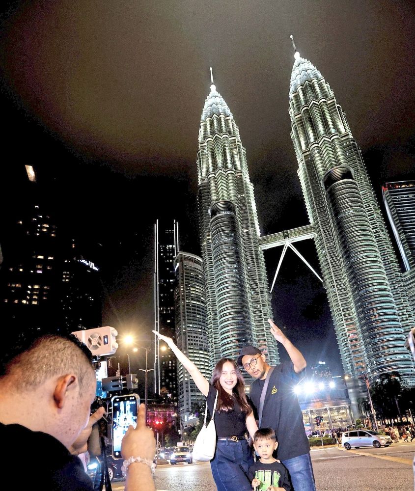 One for the album: A family opting for the services of a foreign roadside photographer to get the perfect shot of the PETRONAS Twin Towers. — CHAN TAK KONG/The Star