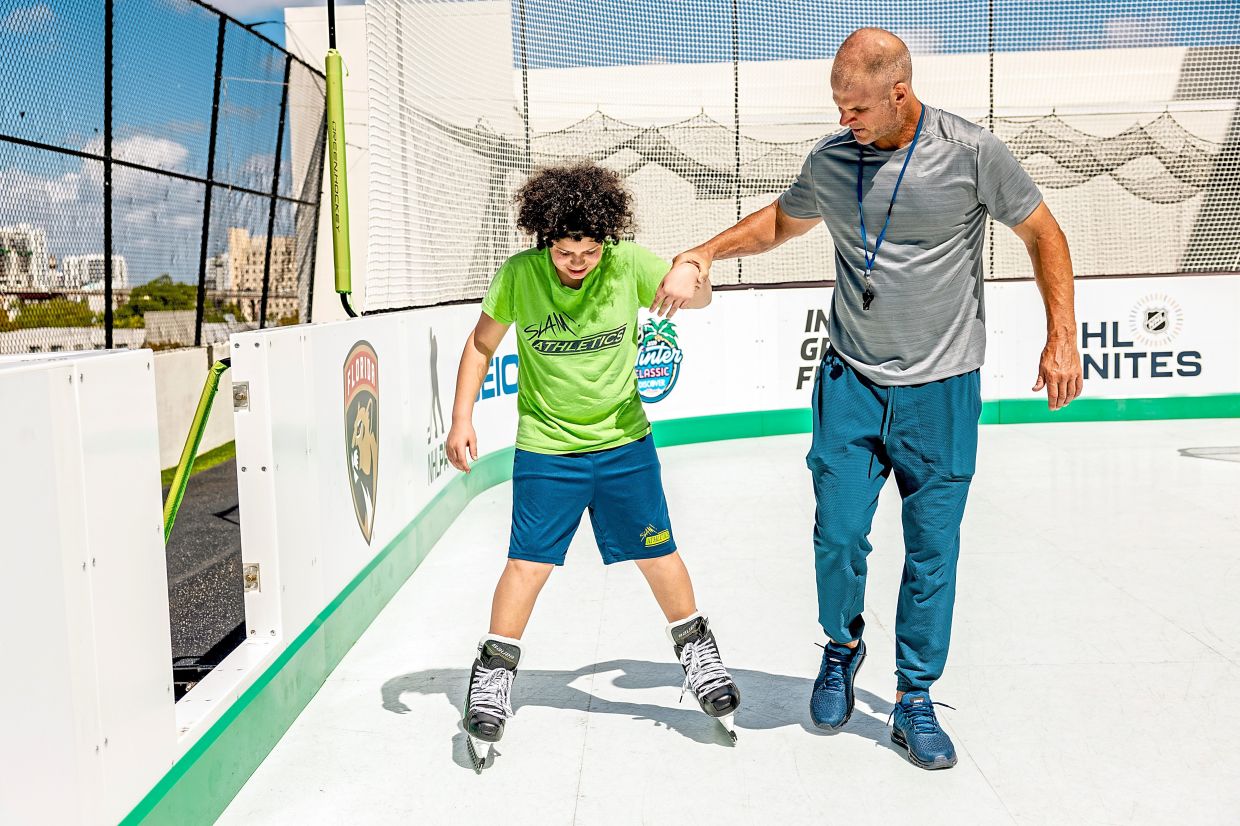 Derek Elvin, a gym teacher, helping Antonio Hayes, 15, skate on specialty skates specificallyfor Slam Miami’s synthetic ice hockey rink. — Scott McIntyre/The New York Times