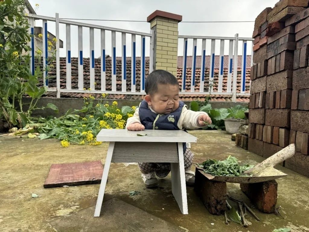Wang squats at a table while helping out in the family’s garden. - Handout via South China Morning Post