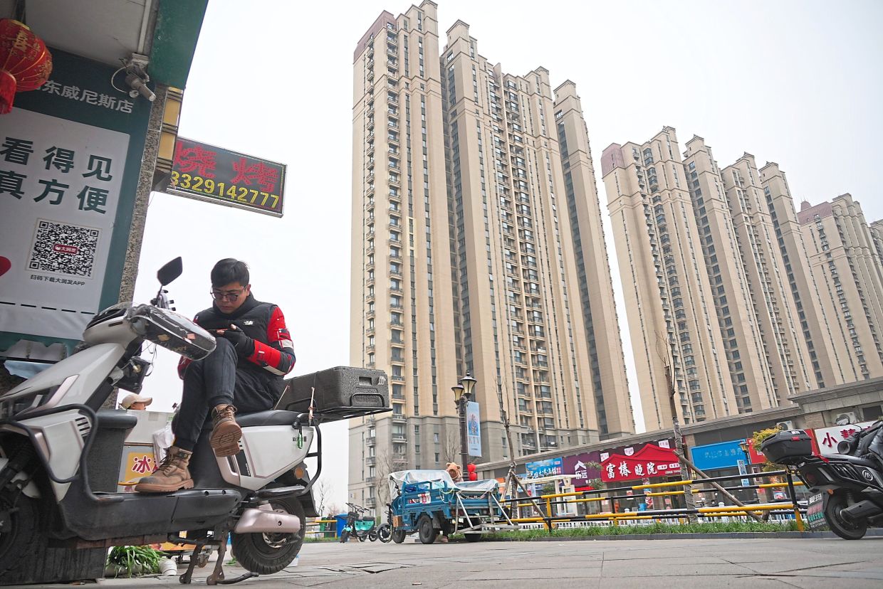 Finding a home: A delivery driver idling away by watching videos on his phone on his scooter. — AP