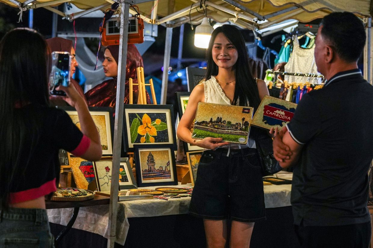 A tourist holds up art pieces by Tom Kim Eng, also known as Aisha, a Cambodian artist who creates art from rice grains, at her stall at a market in Phnom Penh, Cambodia.-- Photo: REUTERS/Soveit Yarn