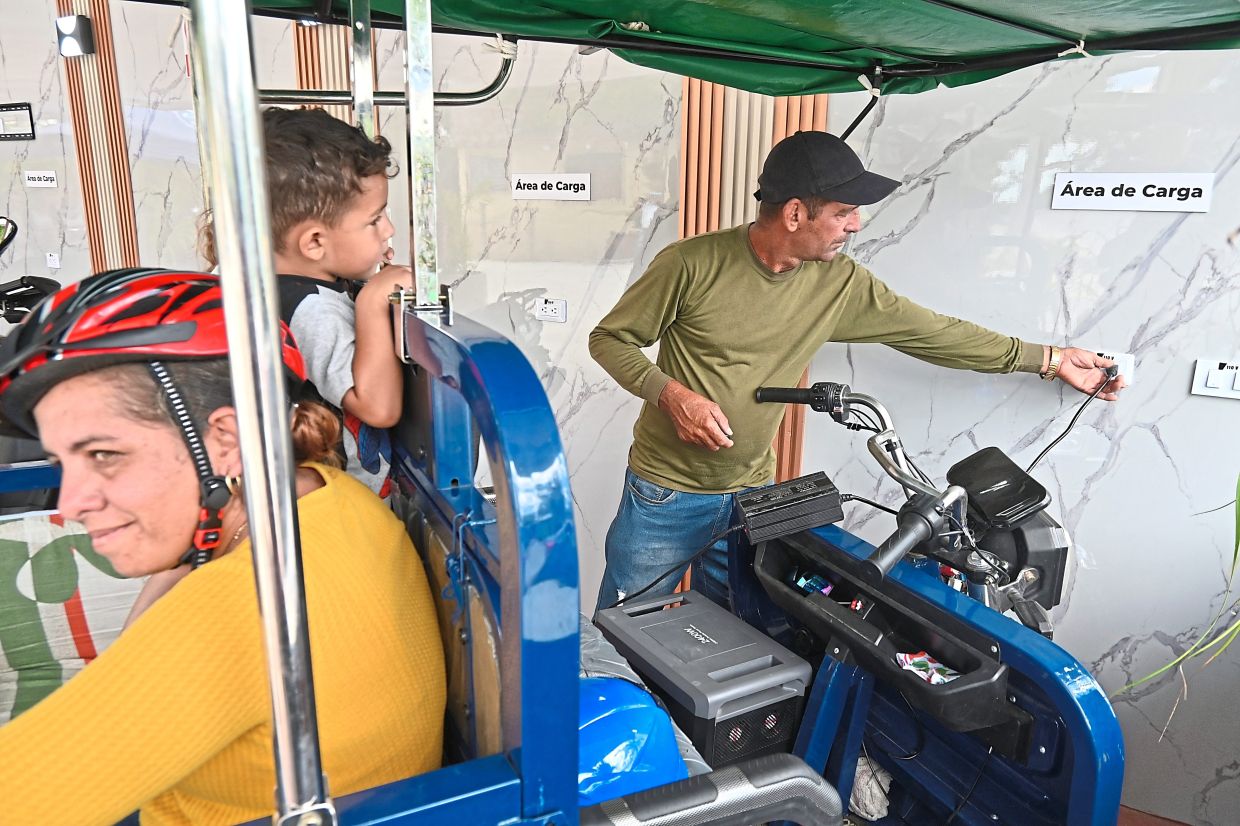 Ravelo (right) plugs in his electric tricycle at a Santa Clara charging station.