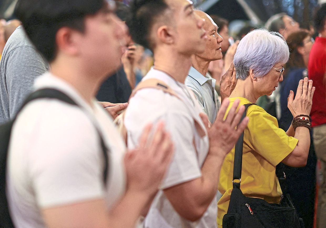 Devotees praying in reverent silence as a giant ‘Wish-Fulfilling shakyamuni Buddha’ thangka – a sacred Tibetan Buddhist scroll depicting the Buddha as an enlightened being believed to bestow spiritual blessings, peace and liberation – is unfurled at Thekchen Choling temple in singapore. — Reuters