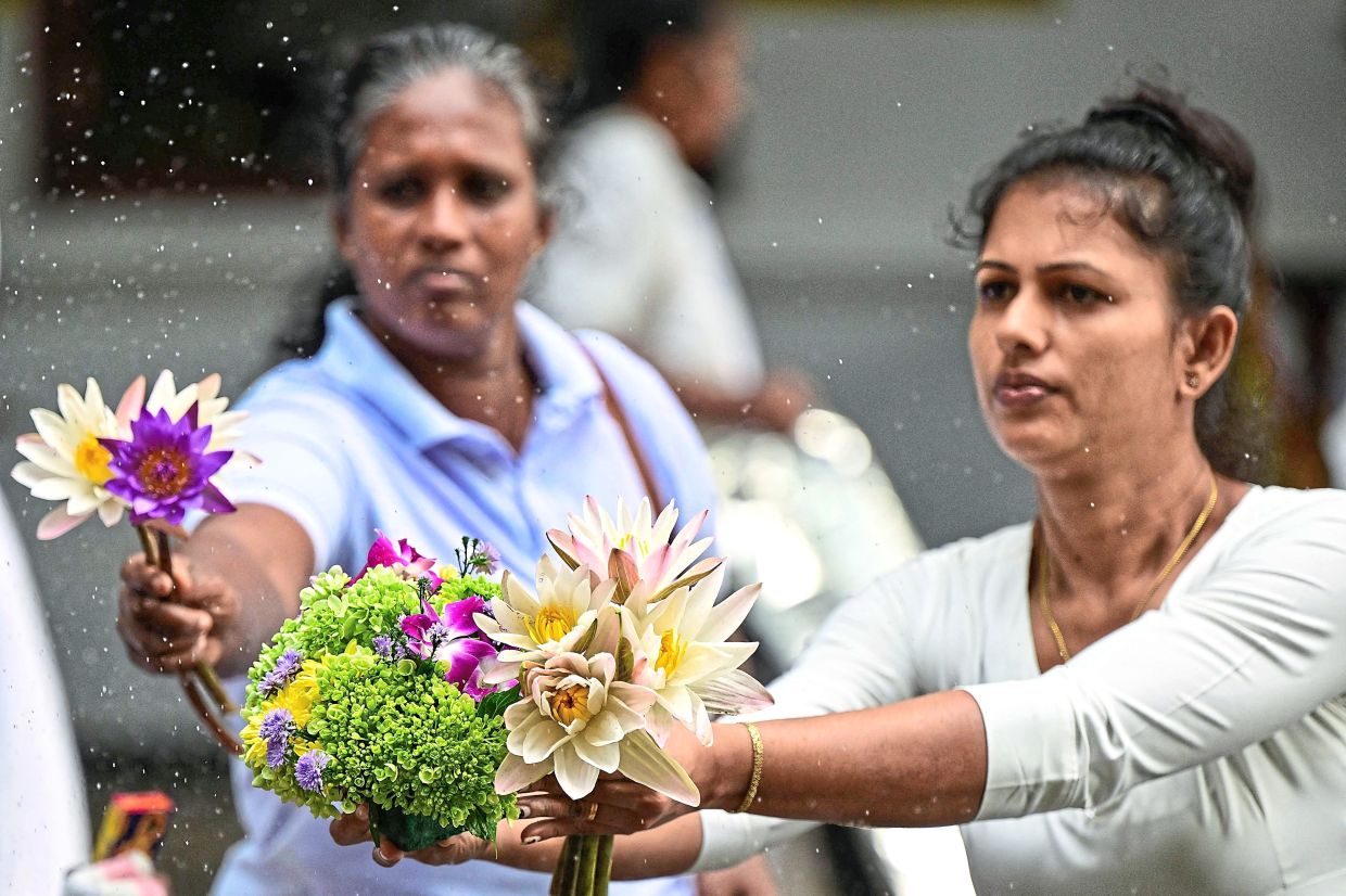 Devotees holding lotus flowers as they offer prayers in devotion at Kelaniya Buddhist Temple in Kelaniya, Sri Lanka. — AFP