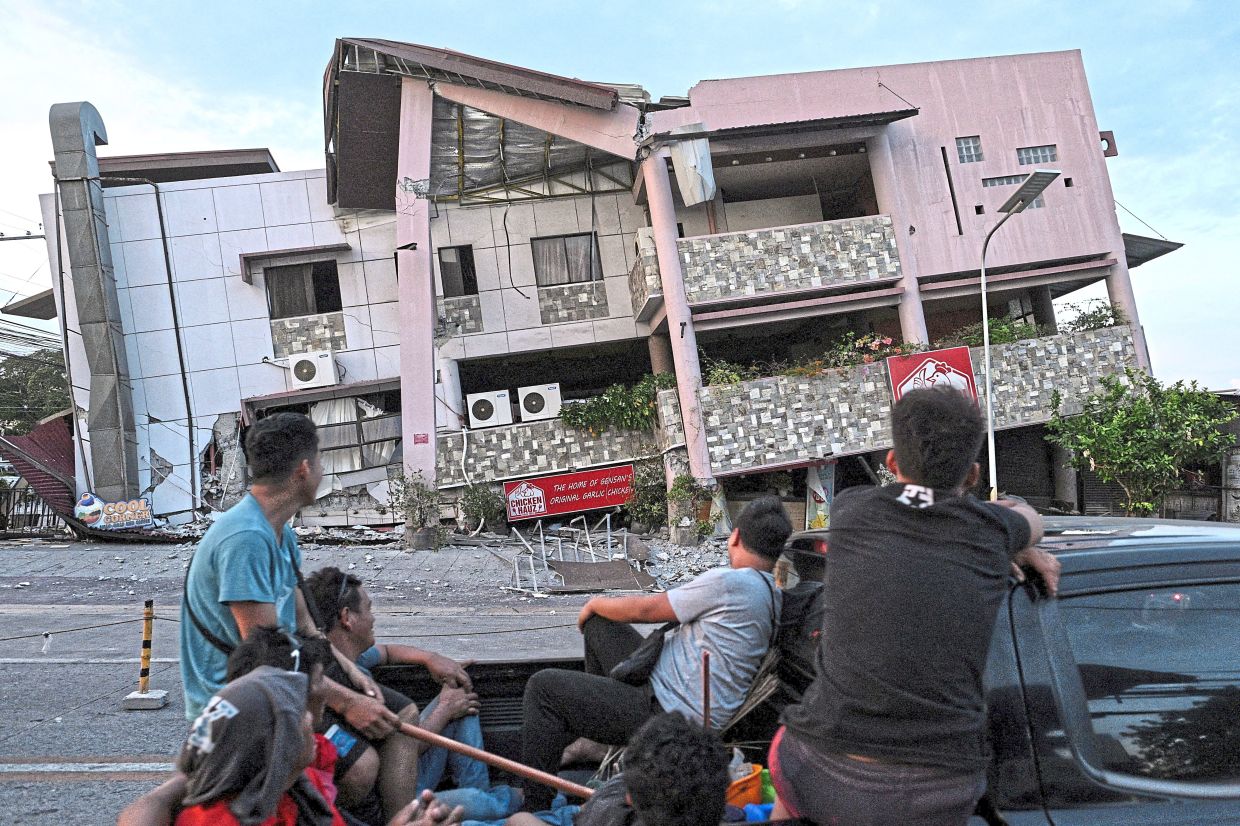 Residents watching in disbelief a partially collapsed building left scarred by the earthquake. — Reuters