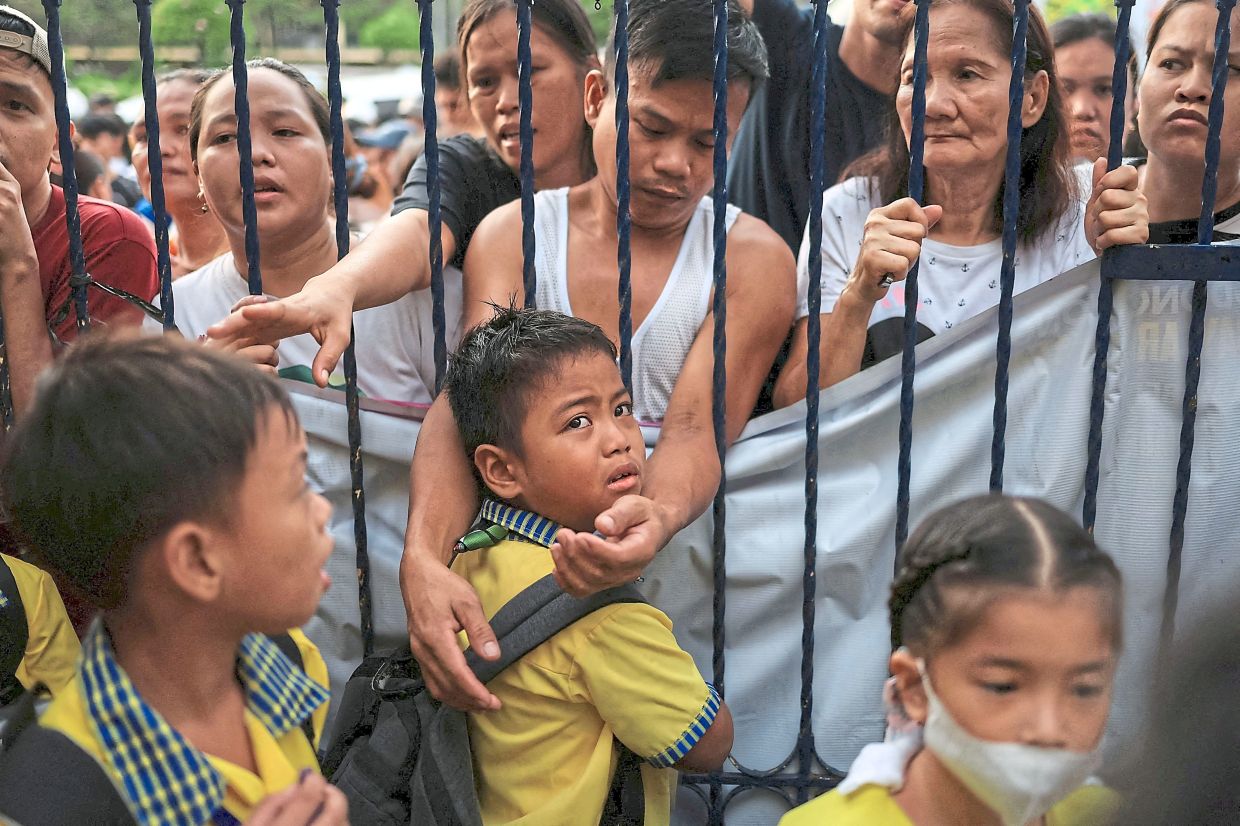 Carlito Villabriga reaching through the school gates to comfort his son, Vien Cael Villabriga, in a poignant reunion after the earthquake at President Corazon C. Aquino Elementary School in Quezon City. — Reuters